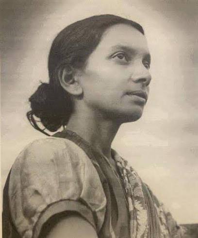 Archival black-and-white photograph of Kalpana Datta in a patterned sari, standing outdoors and looking upward and slightly to her right against an open sky.